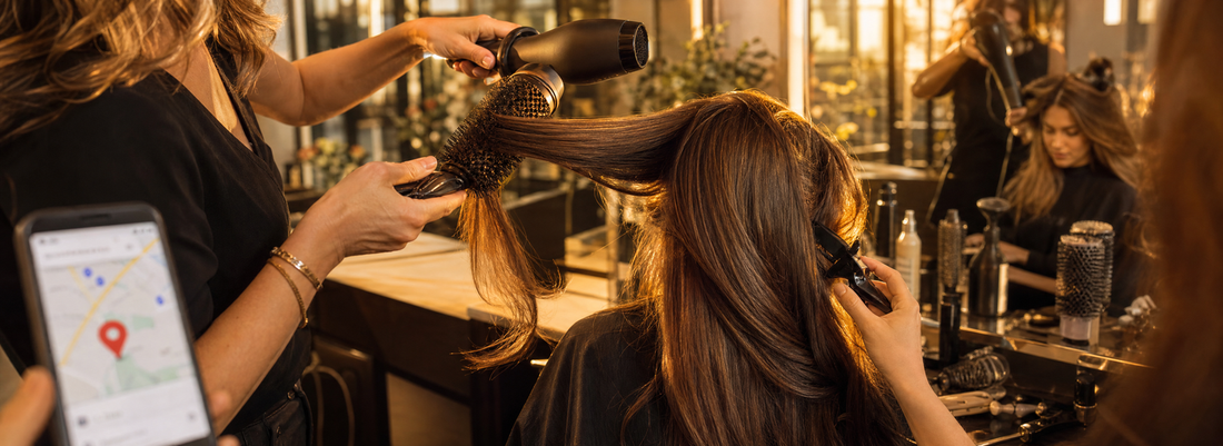 Stylist using a round brush and hair dryer to create a smooth blowout on long hair in a bright professional salon